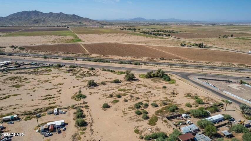 Aerial view of vacant desert land beside a highway, with farmland and mountains beyond.