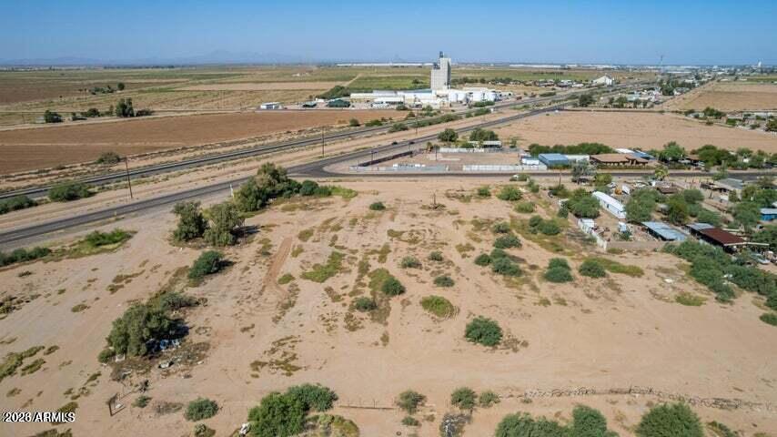 Undeveloped desert parcel with sparse brush near a highway and scattered buildings.