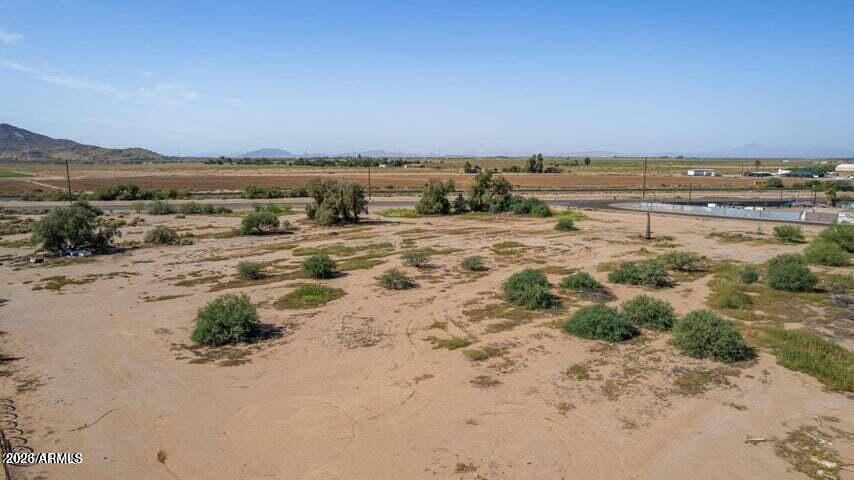 Aerial view of a sandy vacant lot with sparse shrubs and farmland beyond.