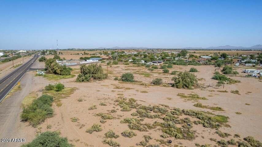 Aerial view of dry desert land beside a paved road, with sparse shrubs and distant homes.