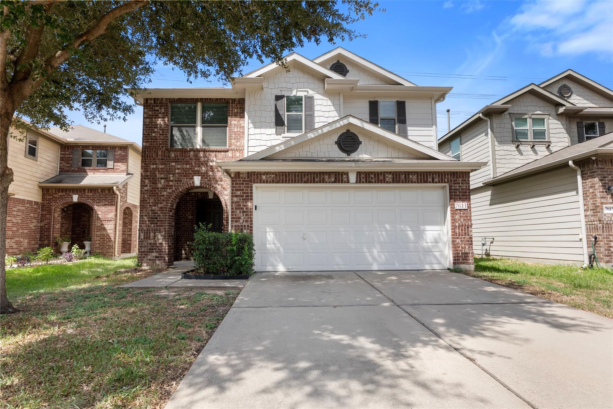 Two-story brick house with a white double garage, arched entry, and shaded driveway.