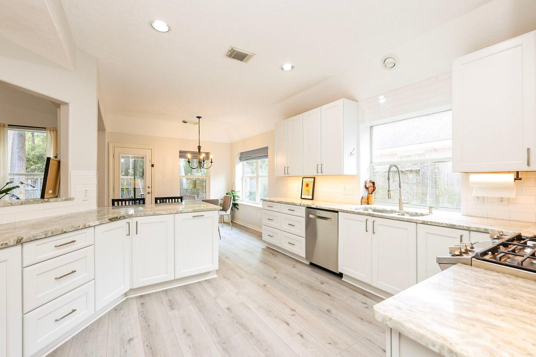 Bright white kitchen with a large stone island, stainless steel appliances, and windows above the sink.
