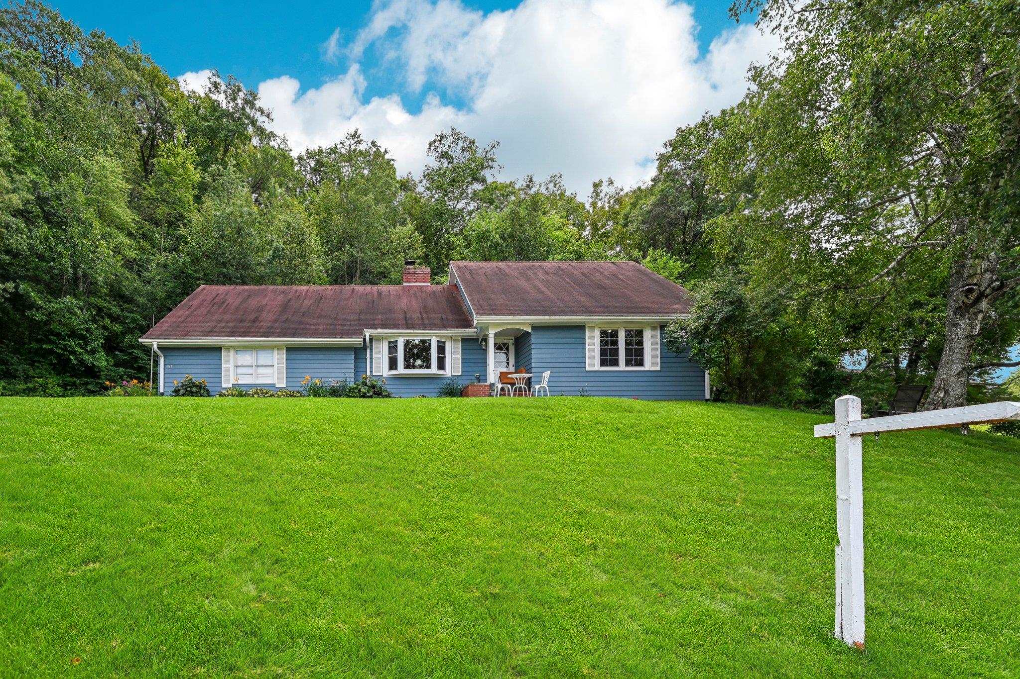 Blue single-story house with white trim, a broad lawn, and mature trees.
