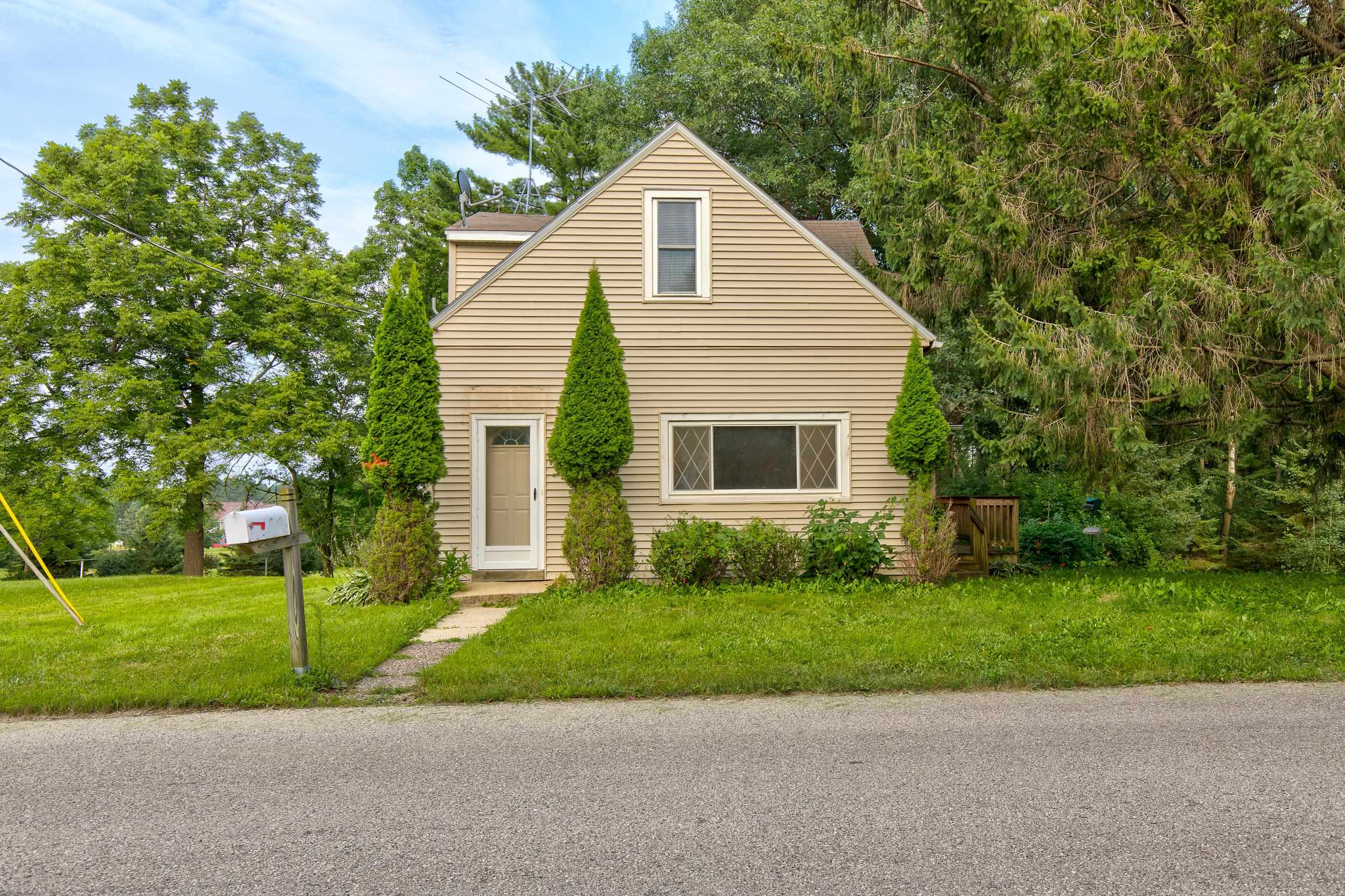 Beige two-story house with a steep gable, evergreen shrubs, and a walkway to the front door.