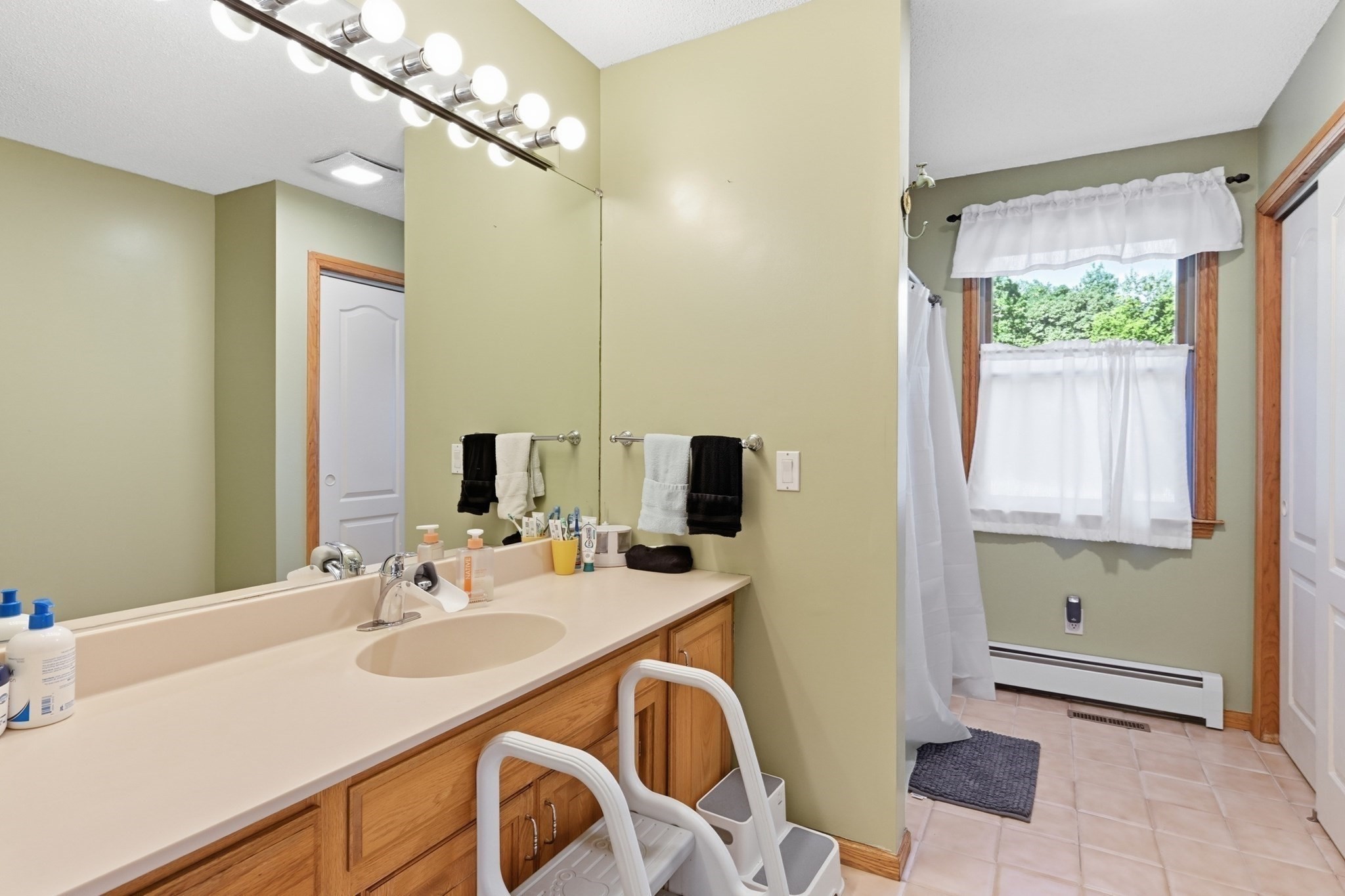 Bathroom with a long wood vanity and large mirror beside a curtained shower and window.