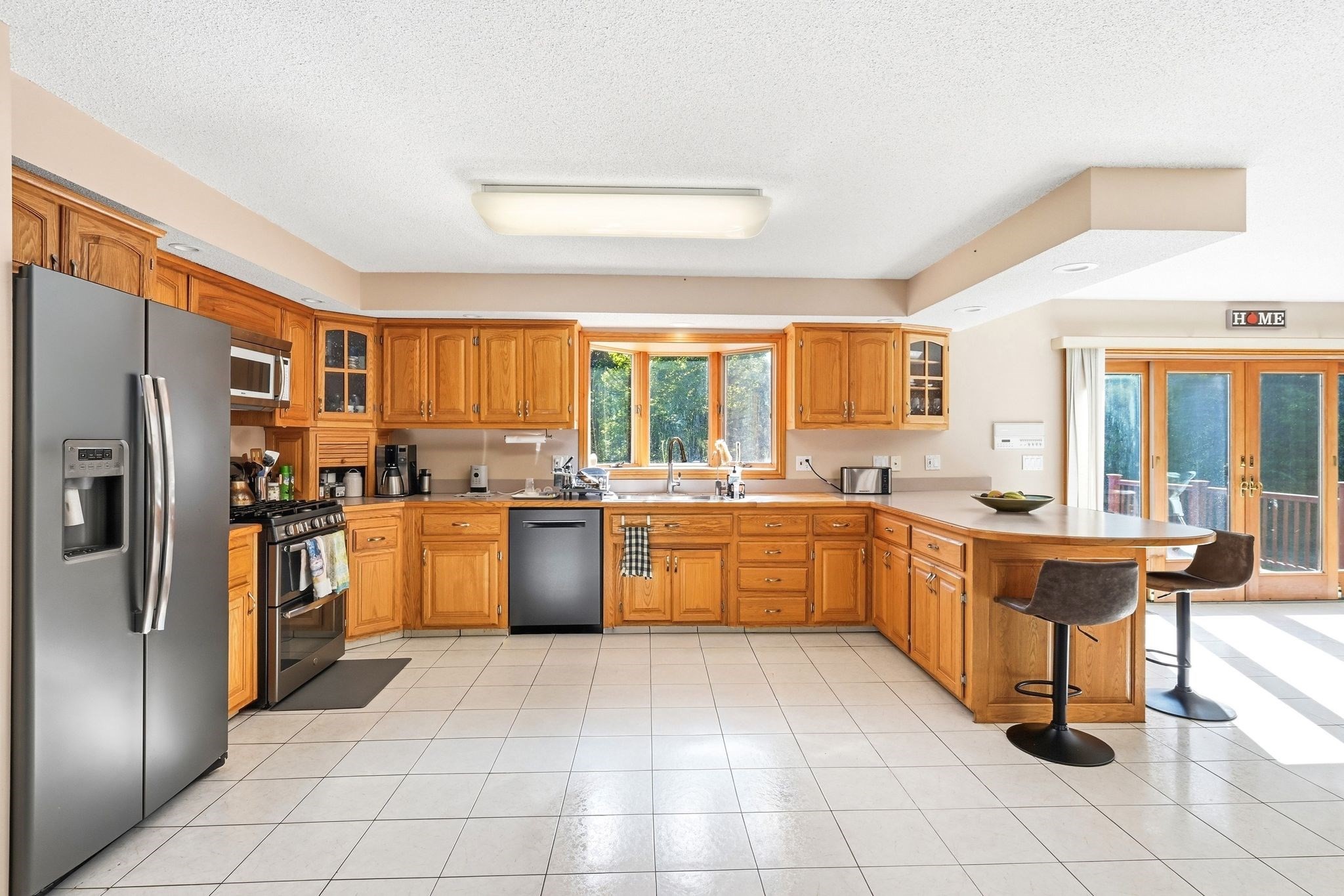 Kitchen with honey-colored wood cabinetry, stainless steel appliances, and a peninsula with bar stools.