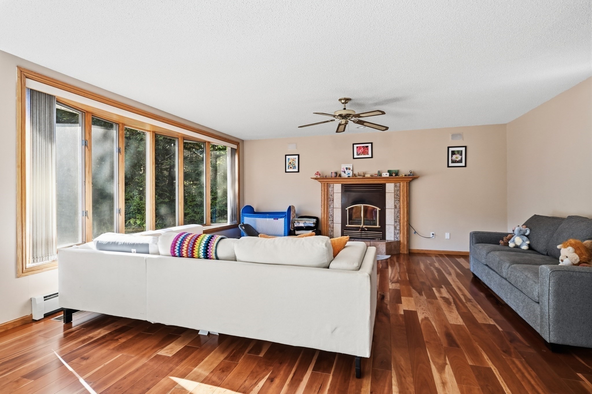 Living room with a fireplace, wide windows, hardwood floors, and white and gray sofas.