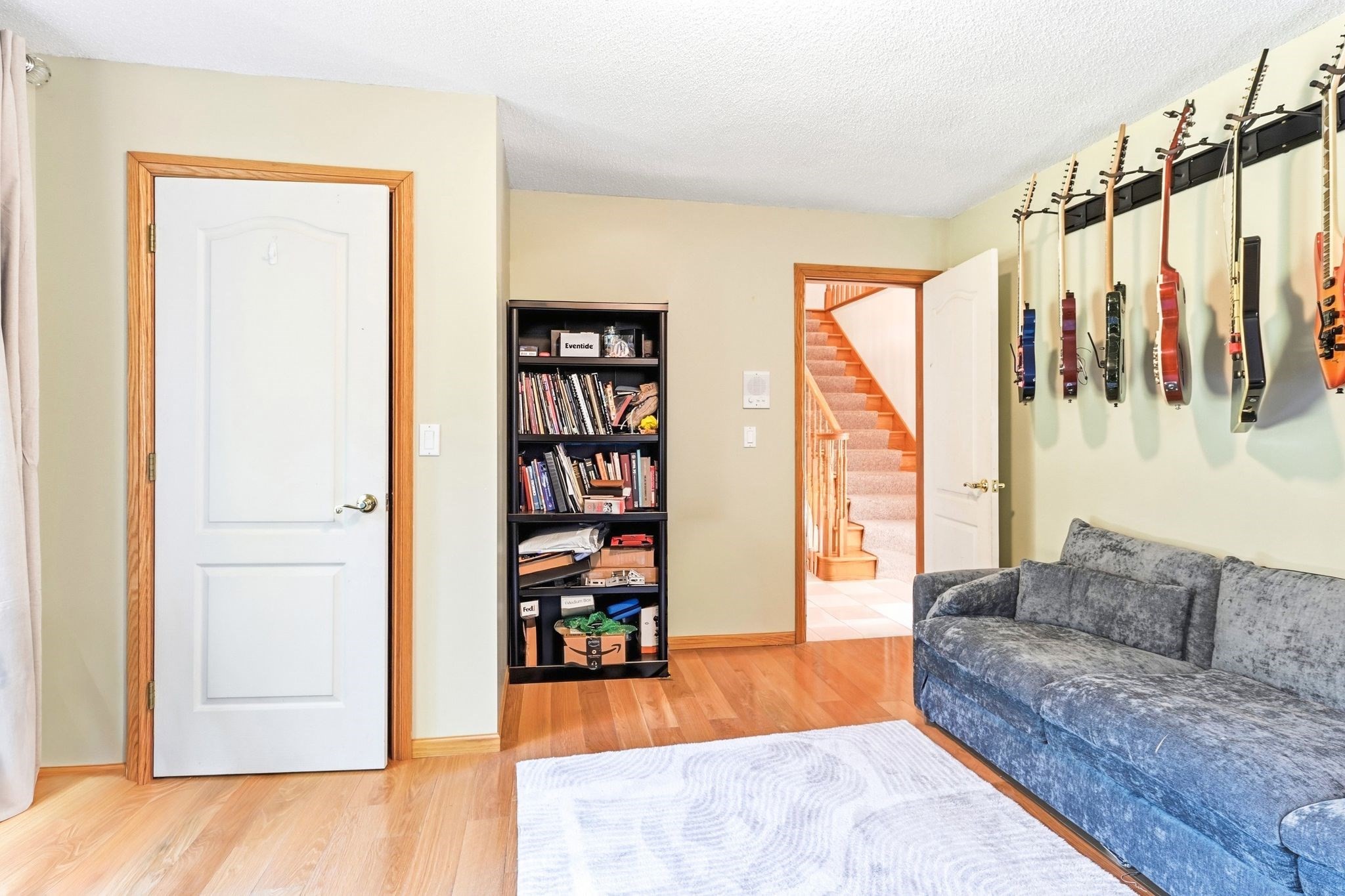 Den with wall-mounted guitars, a gray sofa, bookcase, and doorway to the stairs.