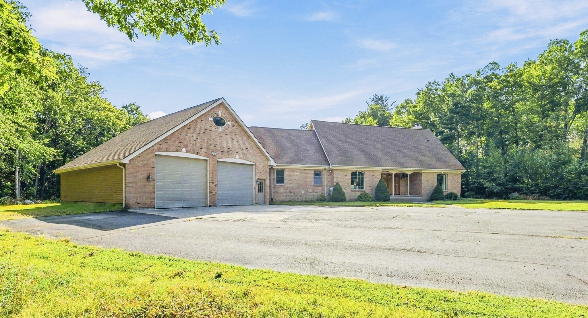 Brick home with a two-car garage, covered entry, and mature trees surrounding the lawn.