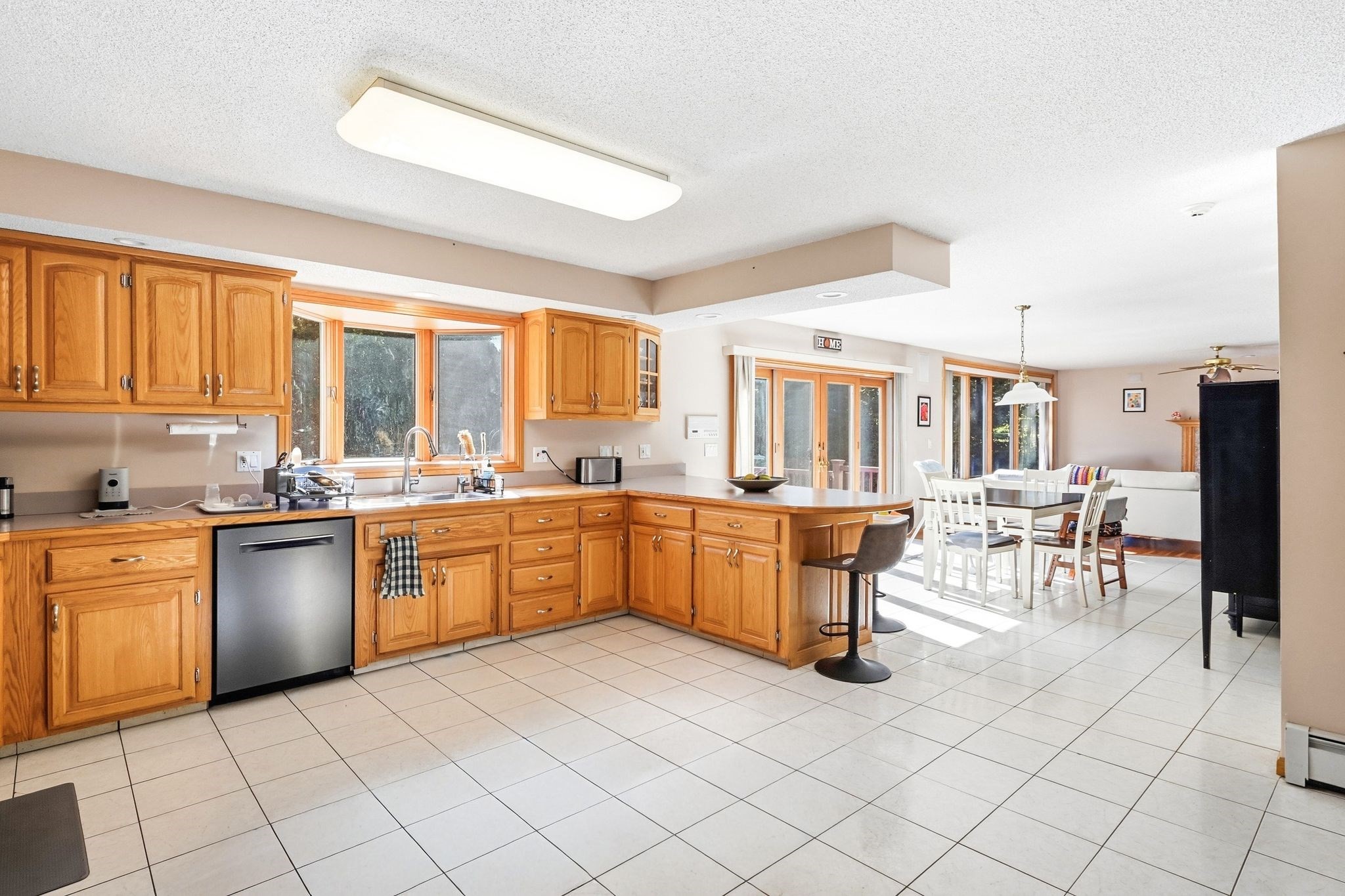 Open kitchen with honey-colored cabinets and island adjoining a sunlit dining area.