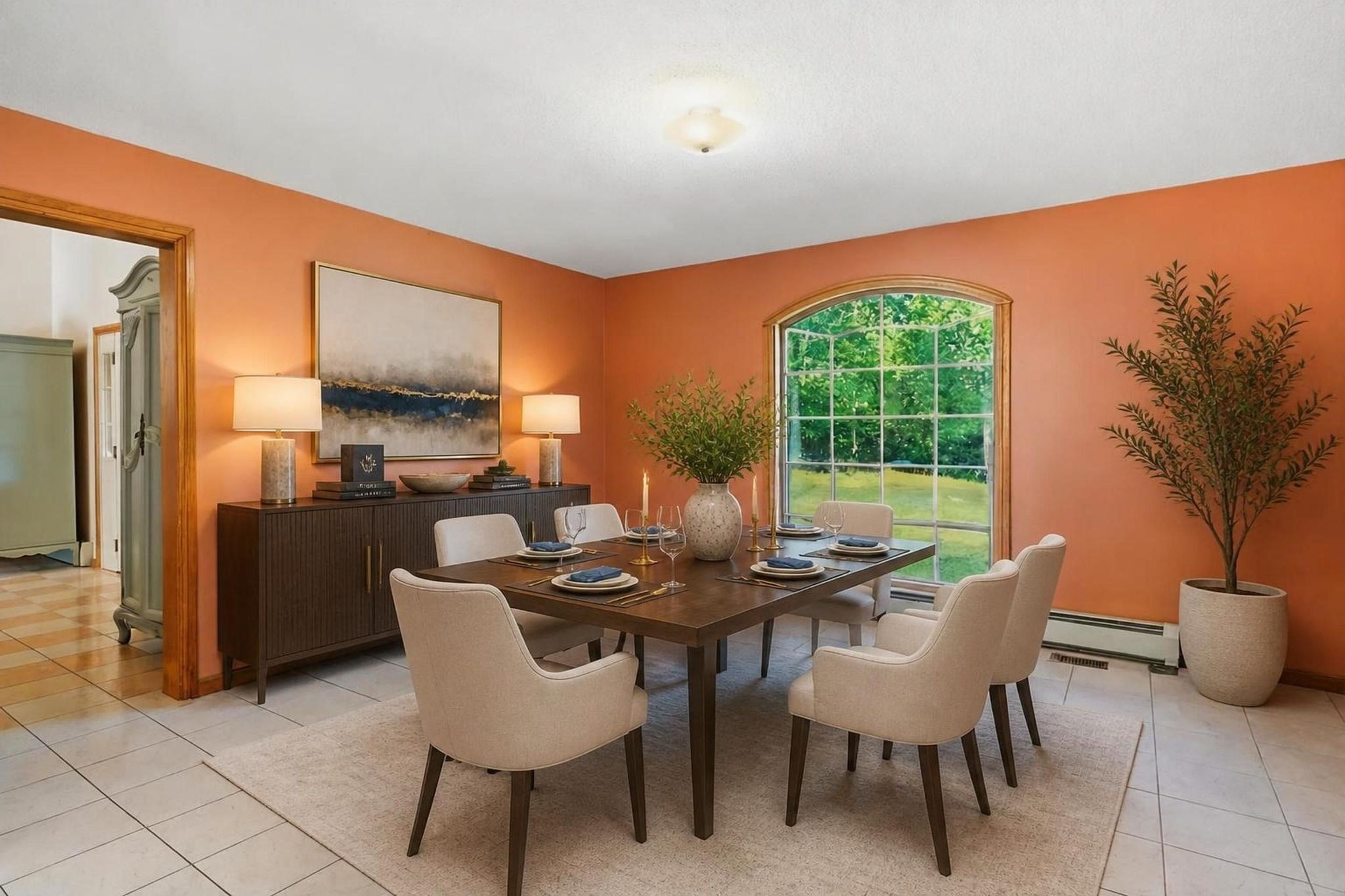 Dining room with orange walls, a dark wood table, cream chairs, and a large arched window.
