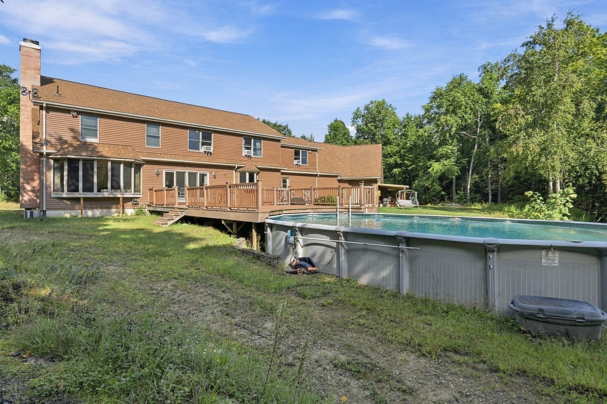 Rear of a brown two-story house with a raised deck, screened porch, and above-ground pool among trees.