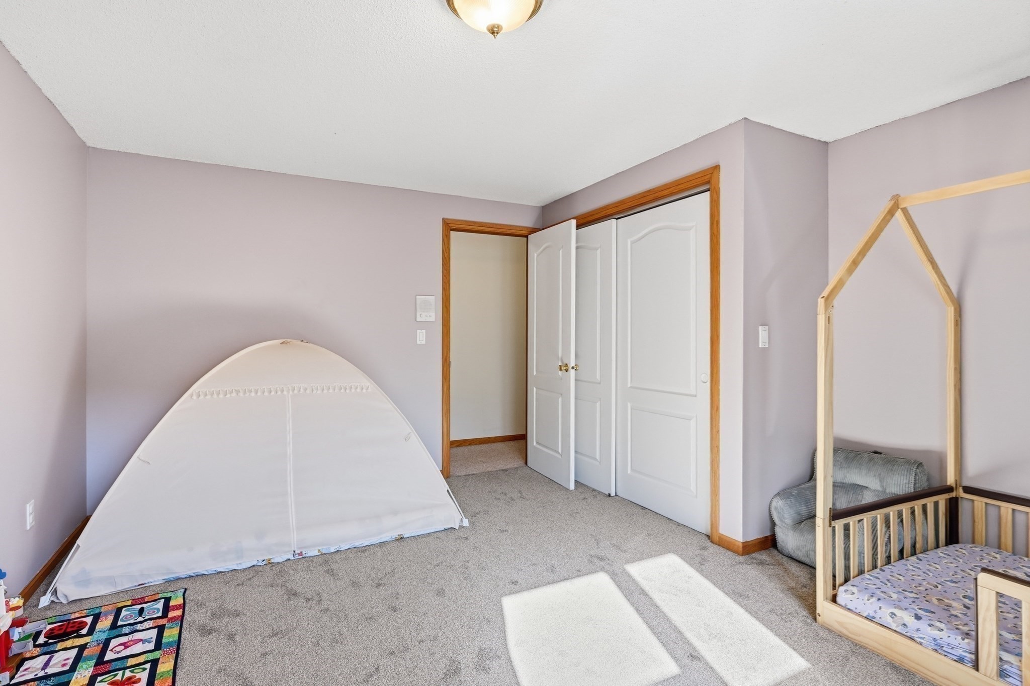 Children’s bedroom with a wooden house-frame bed, white play tent, and colorful play mat.