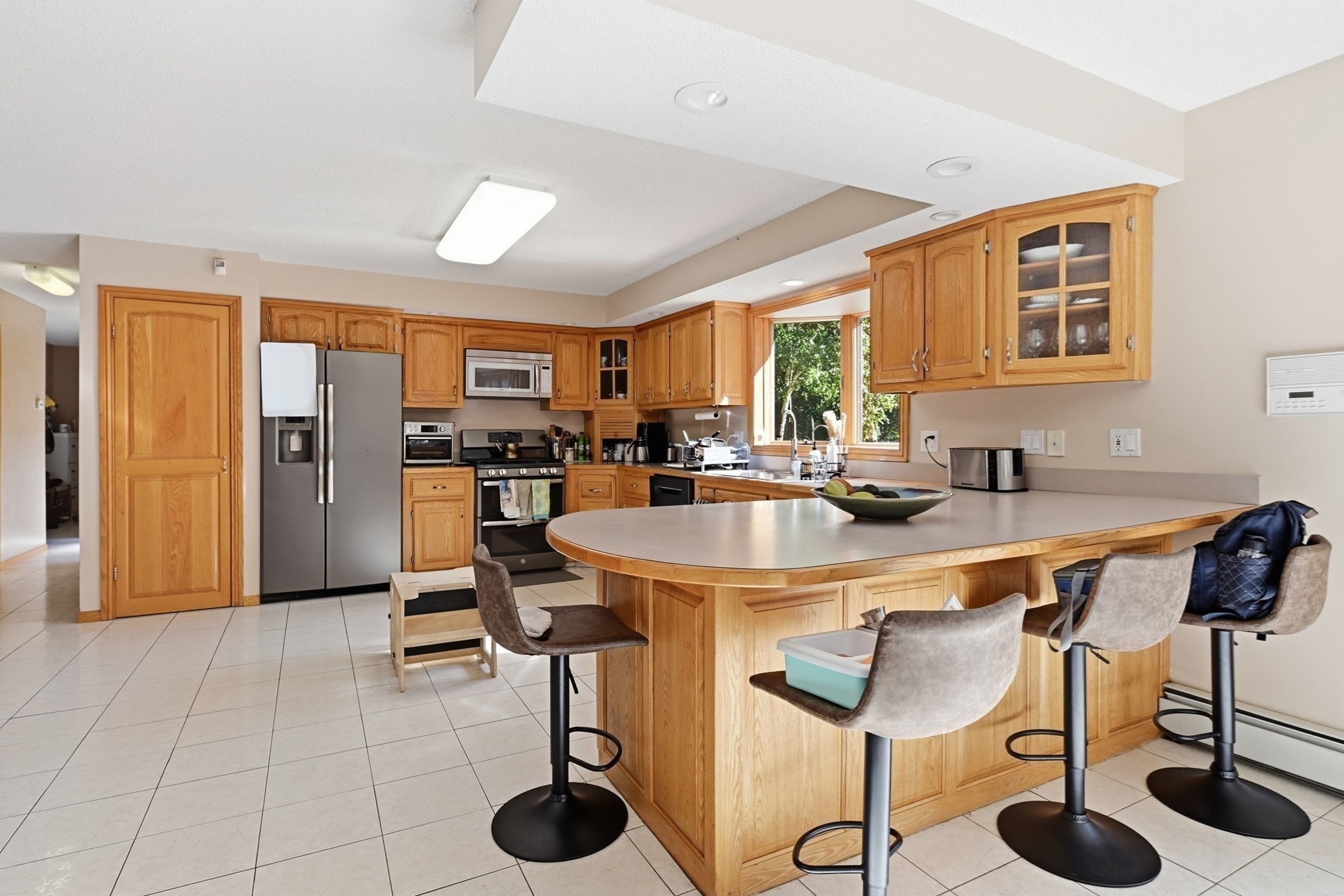 Kitchen with honey-colored cabinets, stainless appliances, and a large island with bar stools.