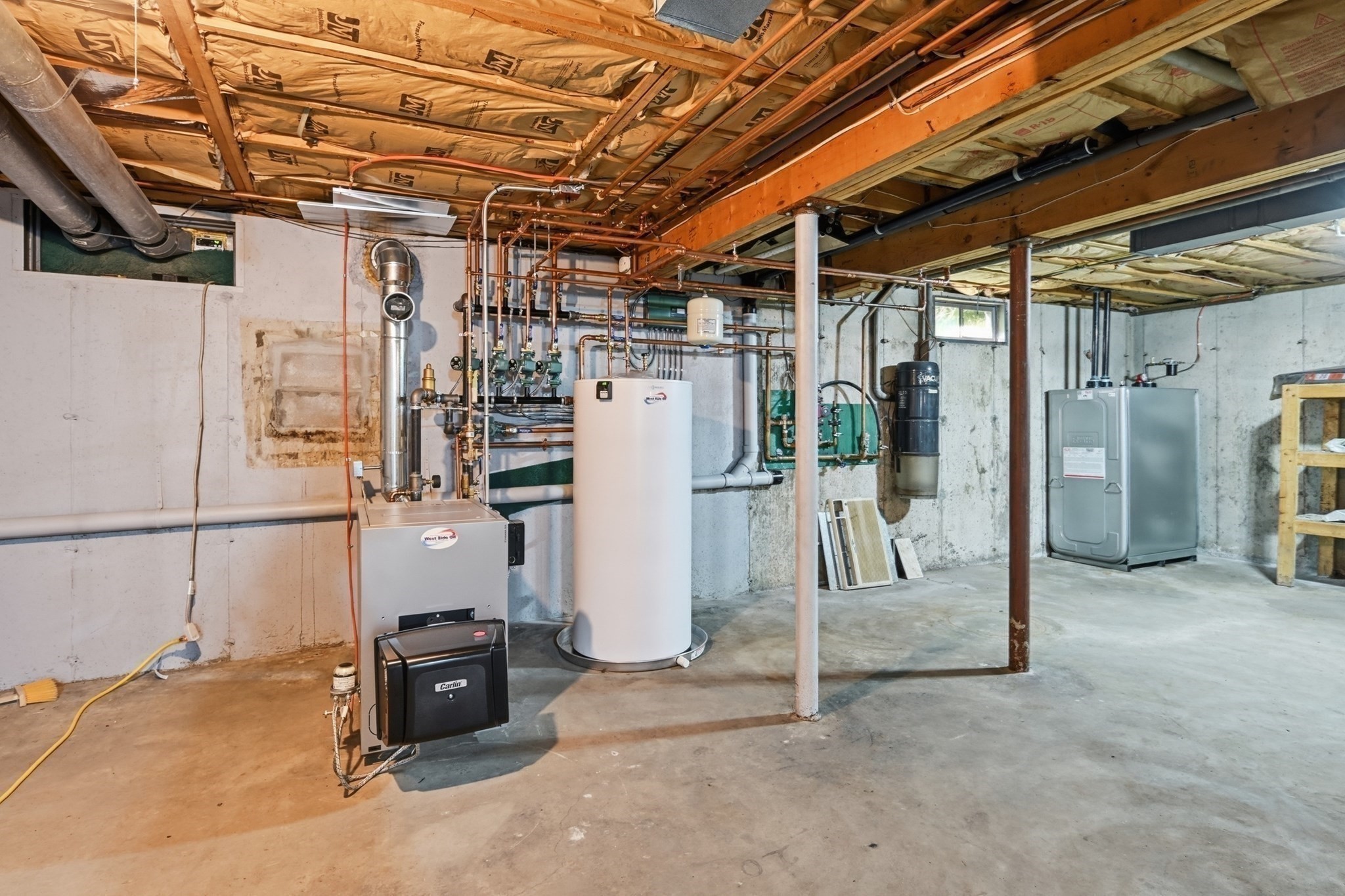 Basement mechanical room with a boiler, water-heater tank, exposed copper pipes, and electrical panel.