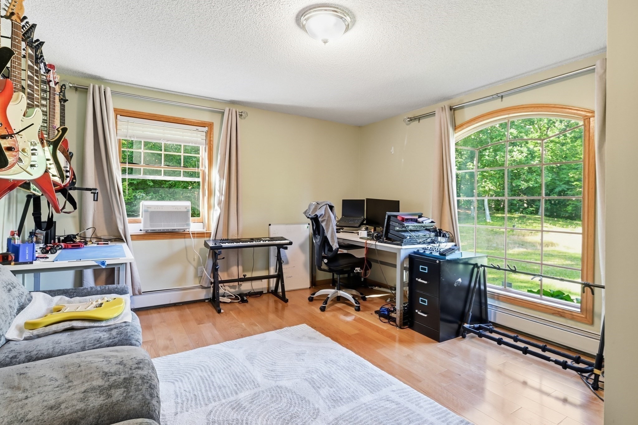 Home music room and office with wall-mounted guitars, recording equipment, and a large arched window.