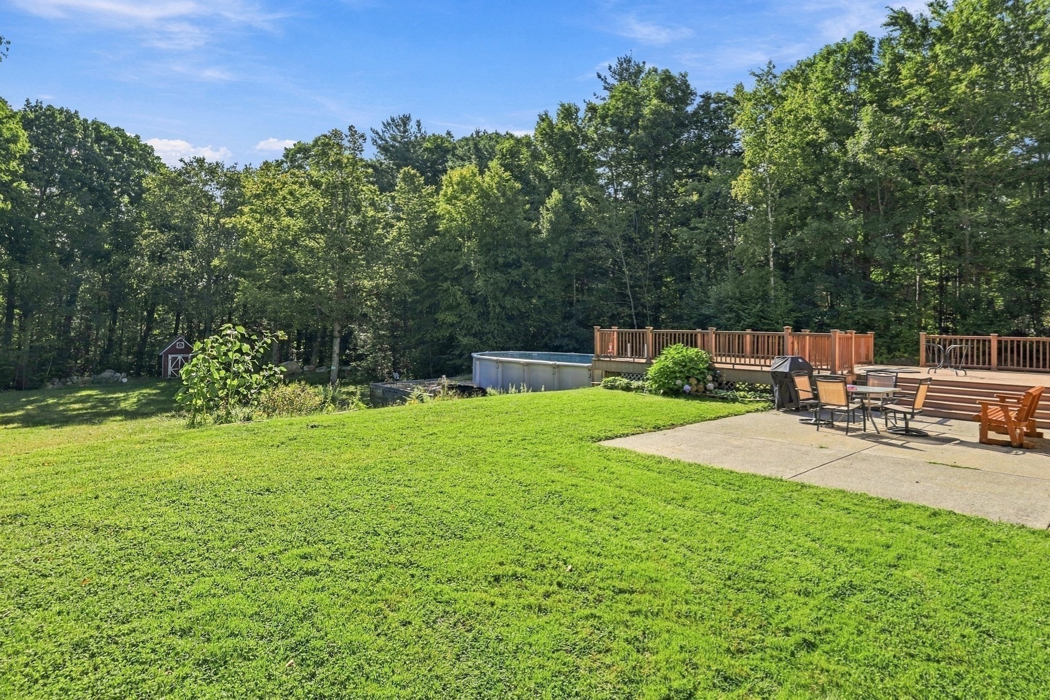Wooded backyard with a wide lawn, above-ground pool, and furnished raised deck.