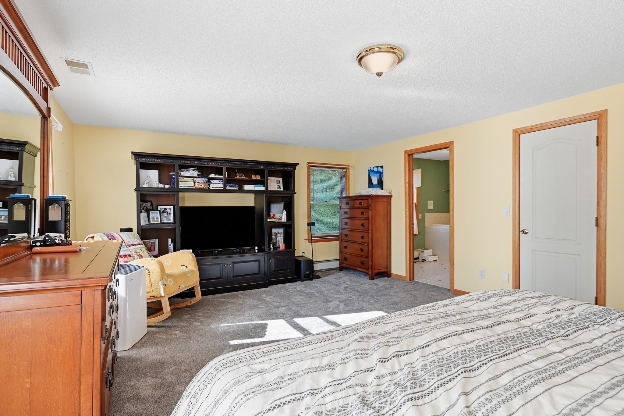 Bedroom with gray carpet, dark built-in media shelving, and a doorway to an adjoining bathroom.