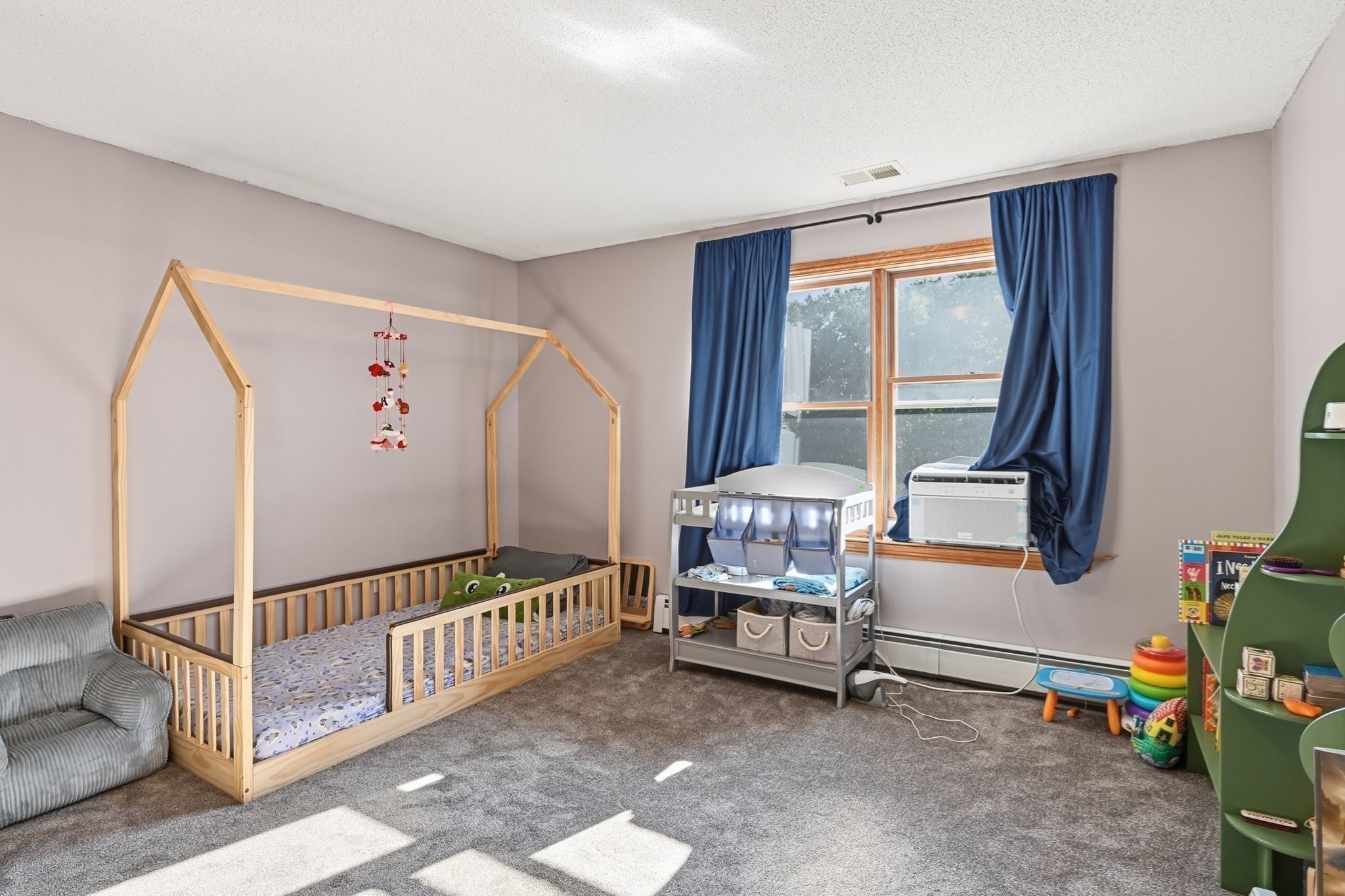 Nursery with a wooden toddler bed, blue curtains, and children's toys.