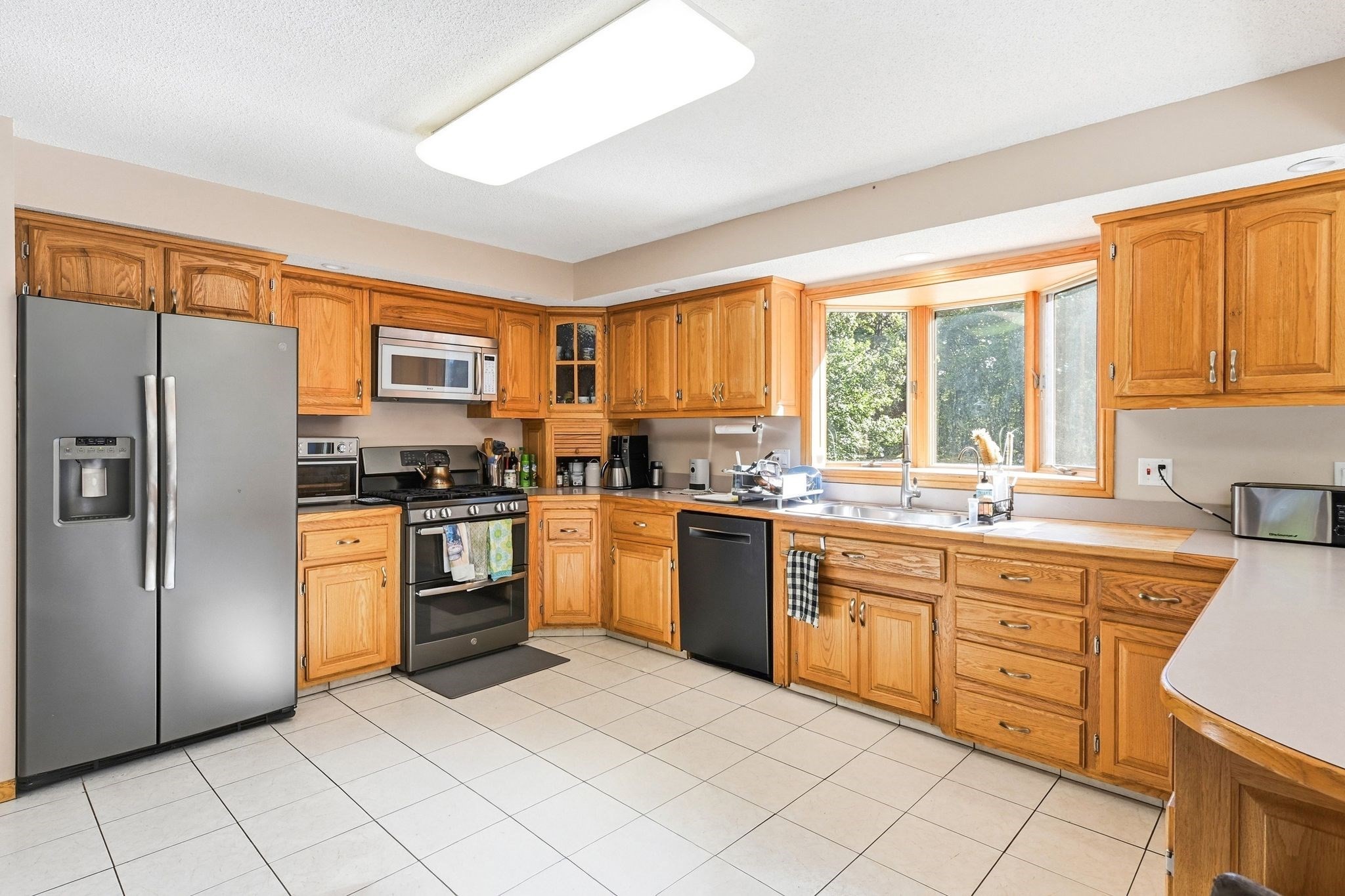 Kitchen with honey-colored wood cabinets, stainless steel appliances, and a wide sunlit window over the sink.