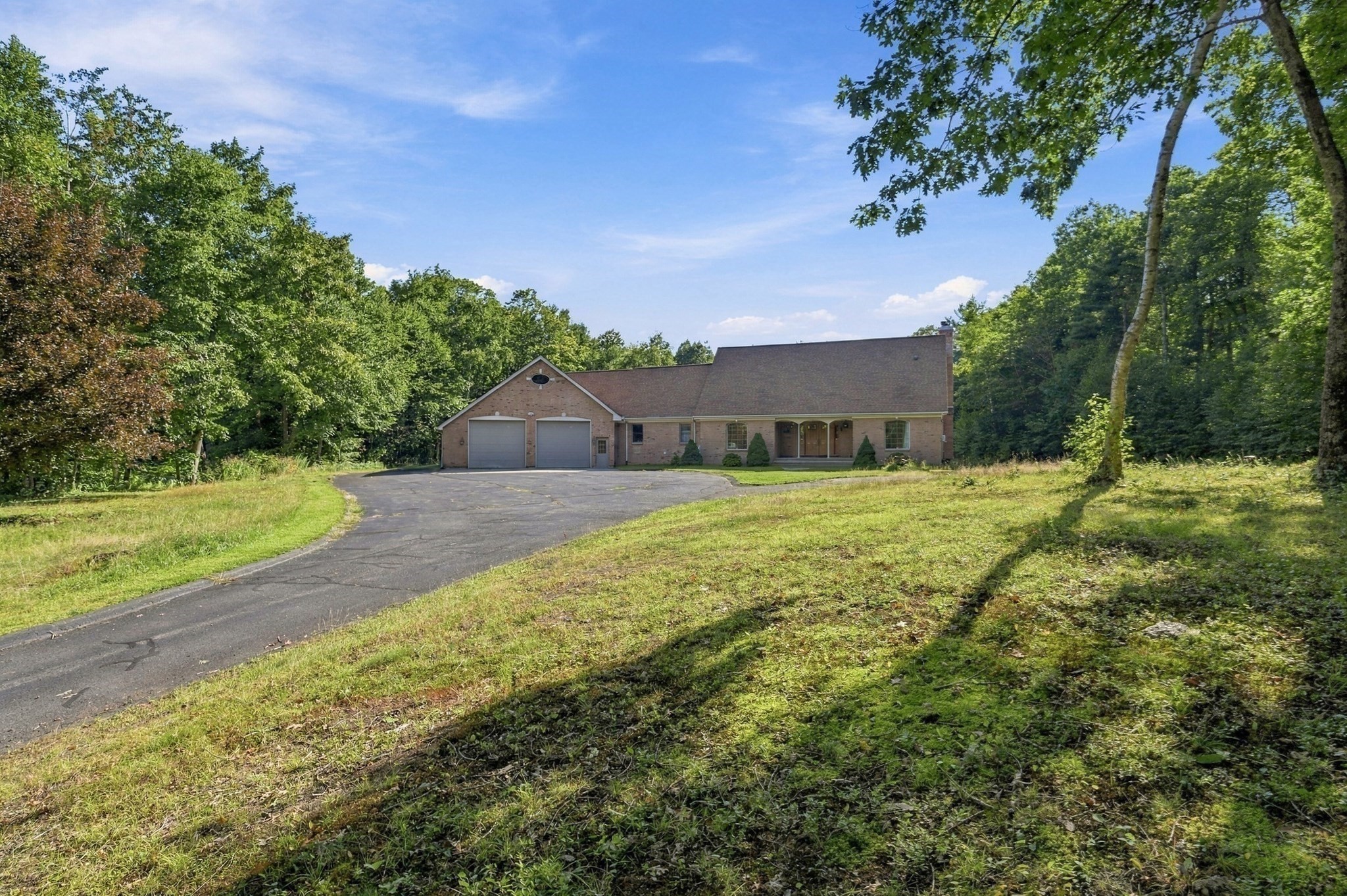 Brick home with two garage doors and a curved driveway amid mature trees.