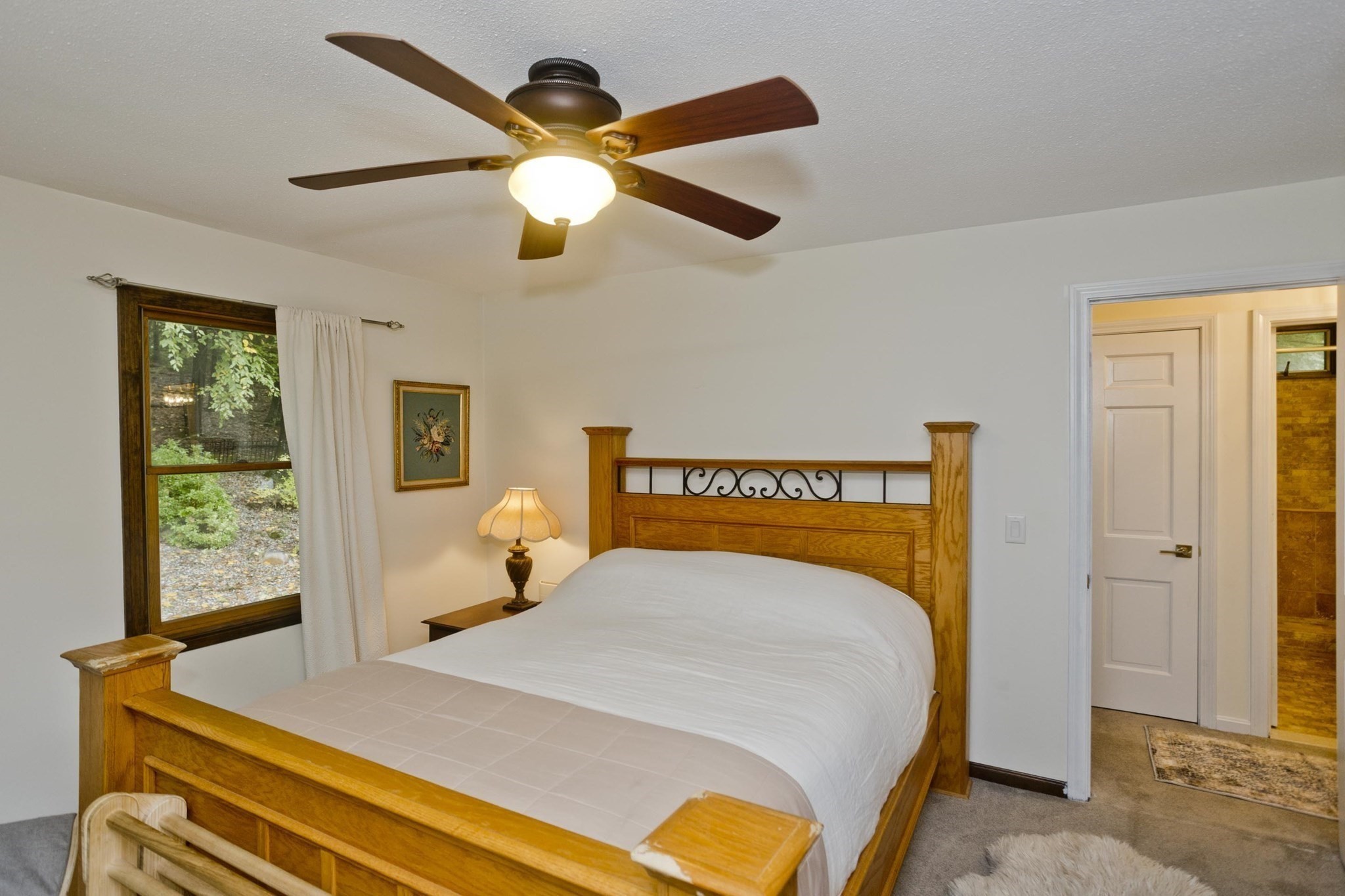 Bedroom with a large wooden bed, ceiling fan, and window overlooking greenery.
