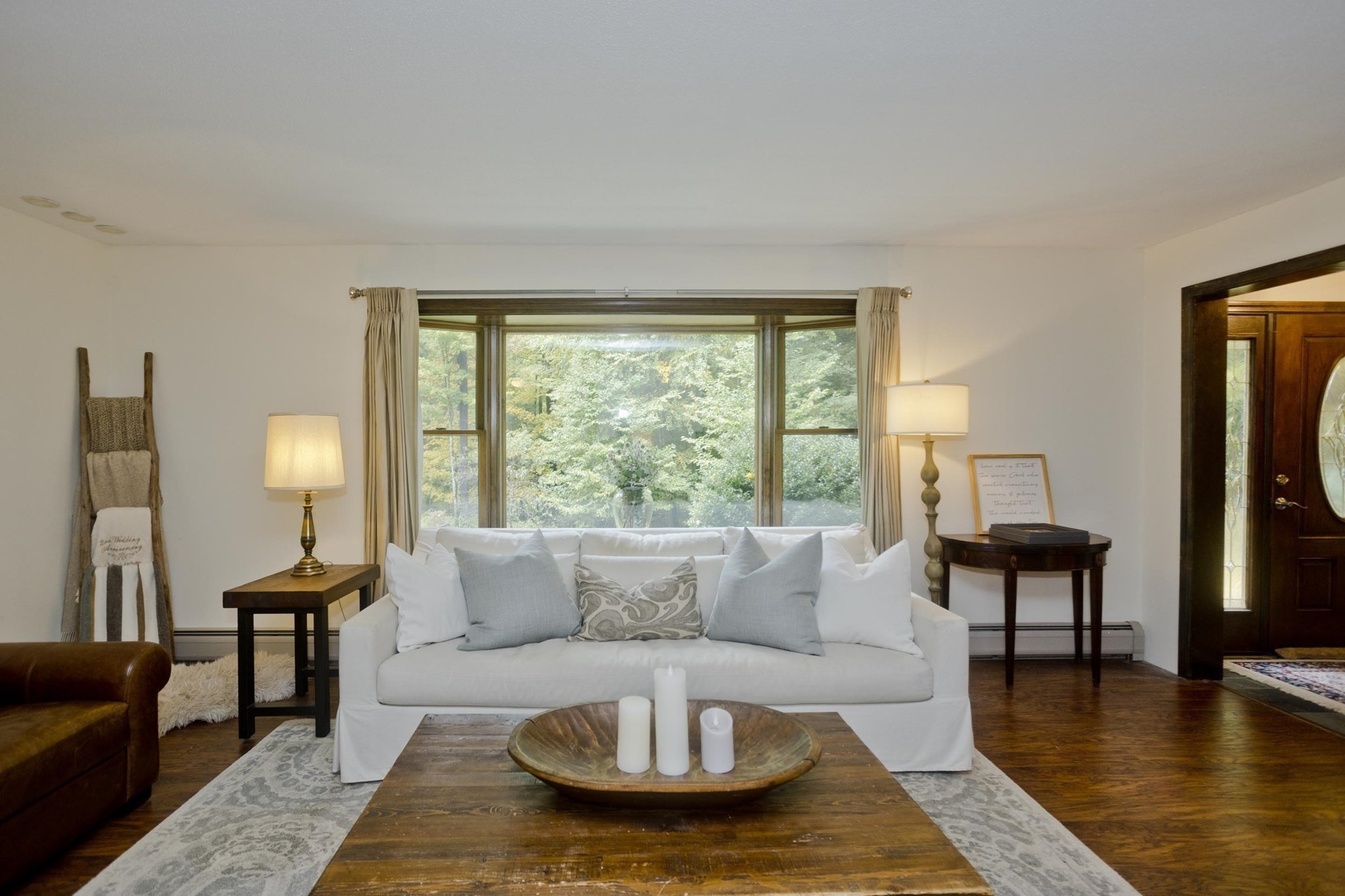 Living room with a white sofa beneath a wide window overlooking leafy trees.