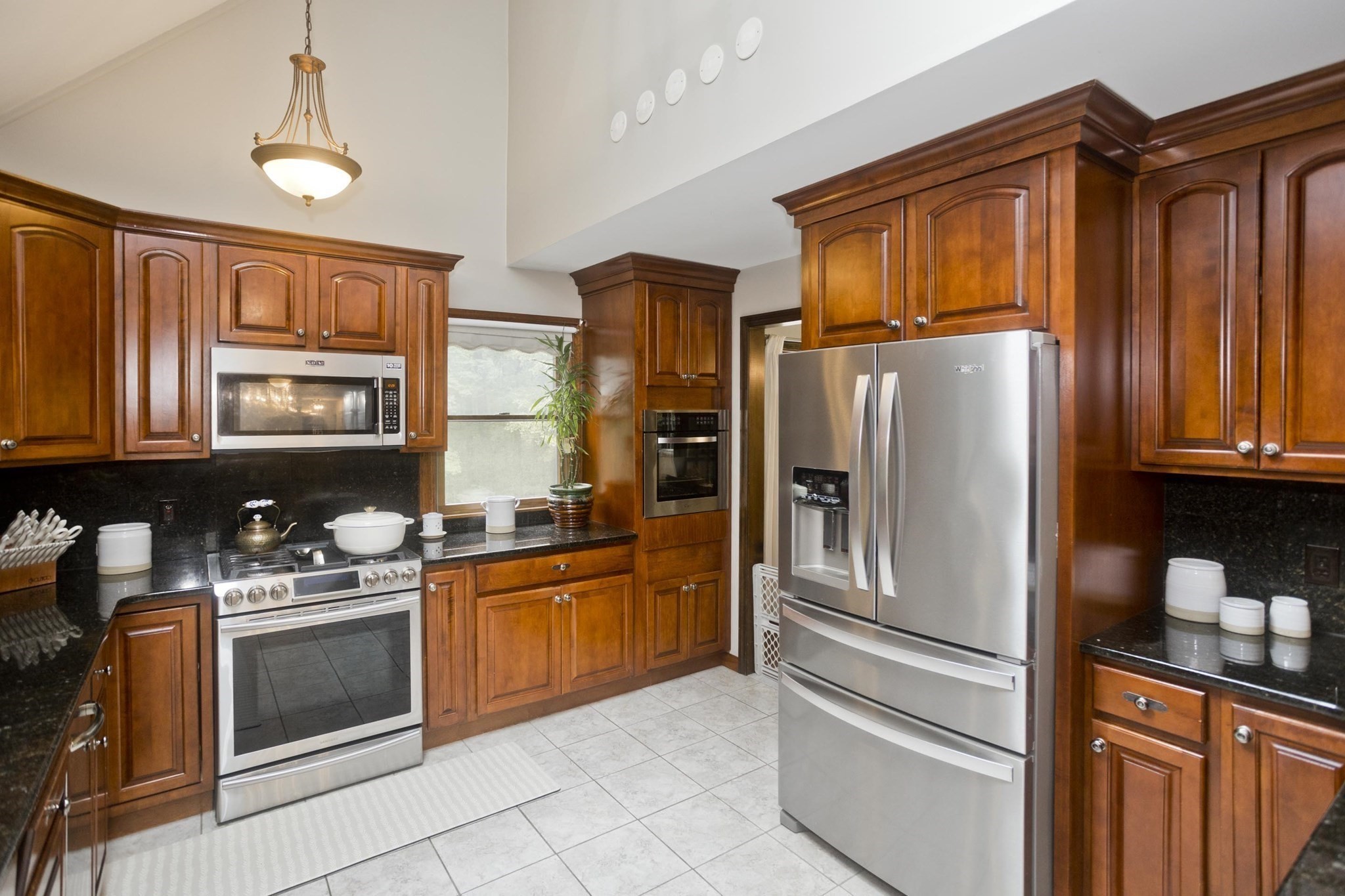 Kitchen with cherry cabinetry, black counters, stainless steel appliances, and light tile flooring.