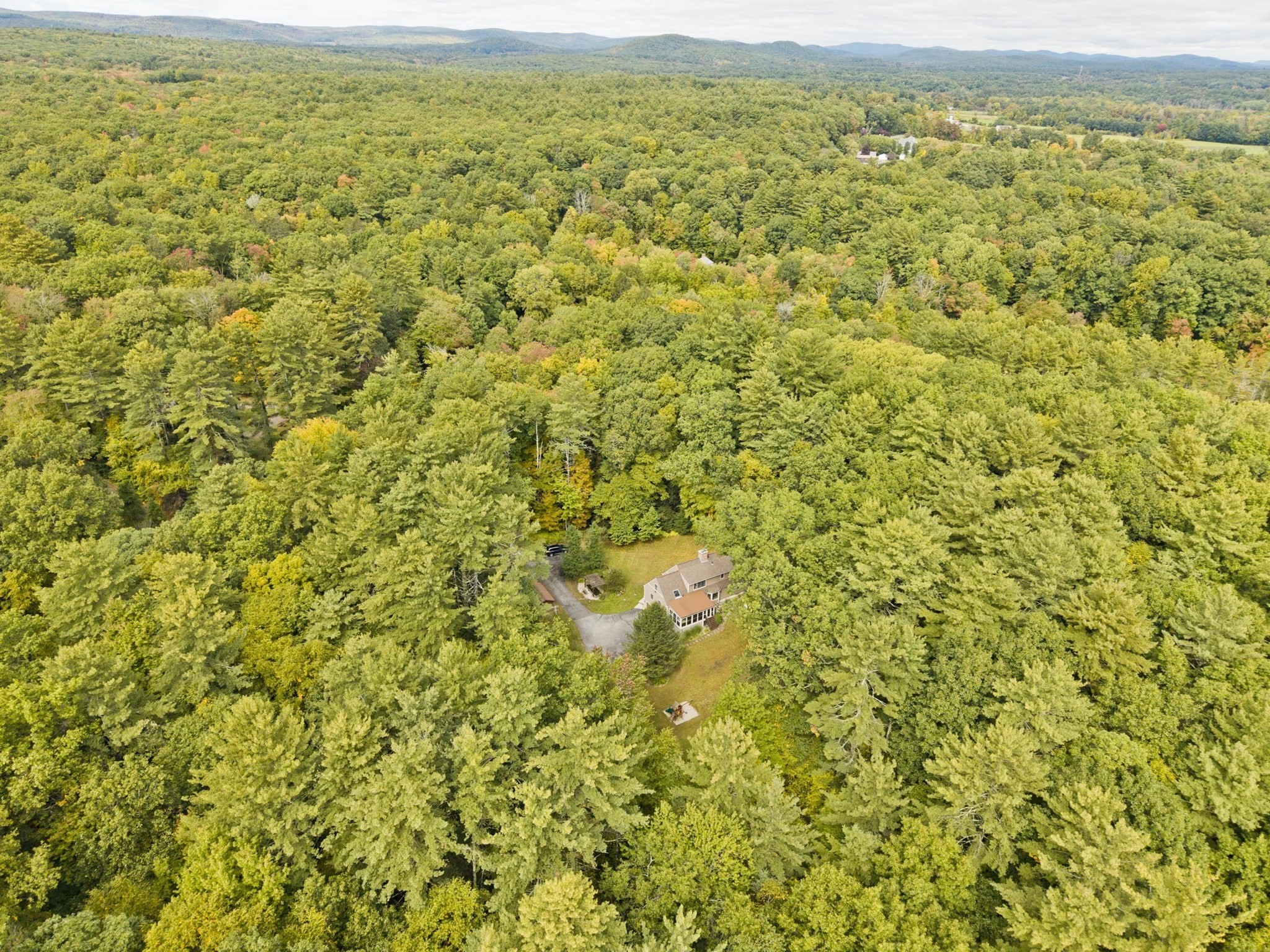 Aerial view of a house nestled in dense woodland, with rolling hills in the distance.