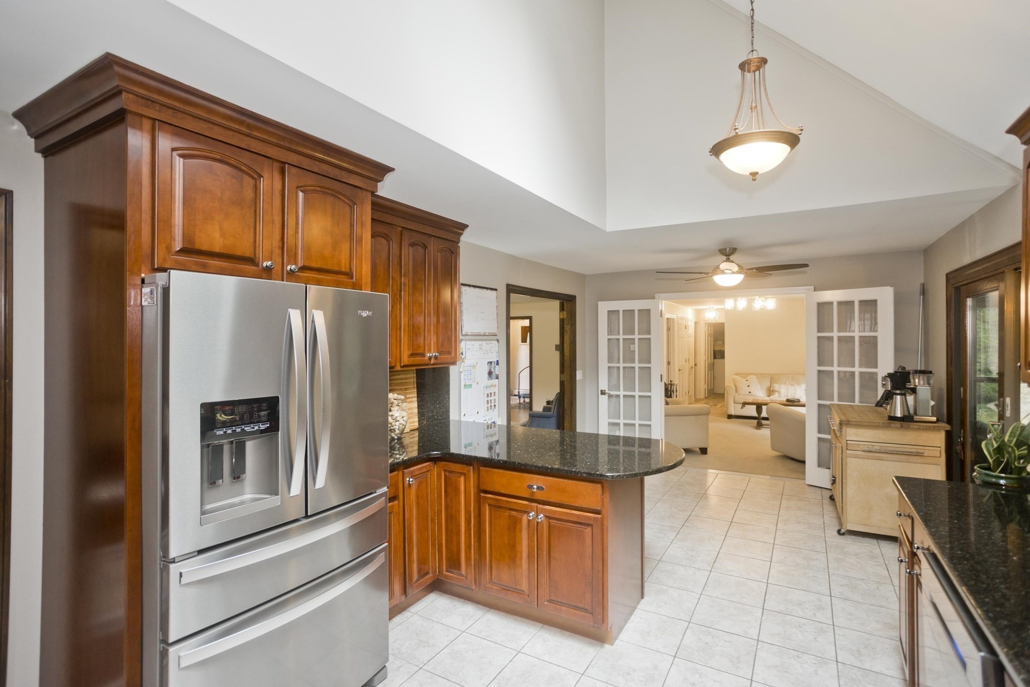 Kitchen with wood cabinetry, stainless steel refrigerator, and granite island opening to the living room.