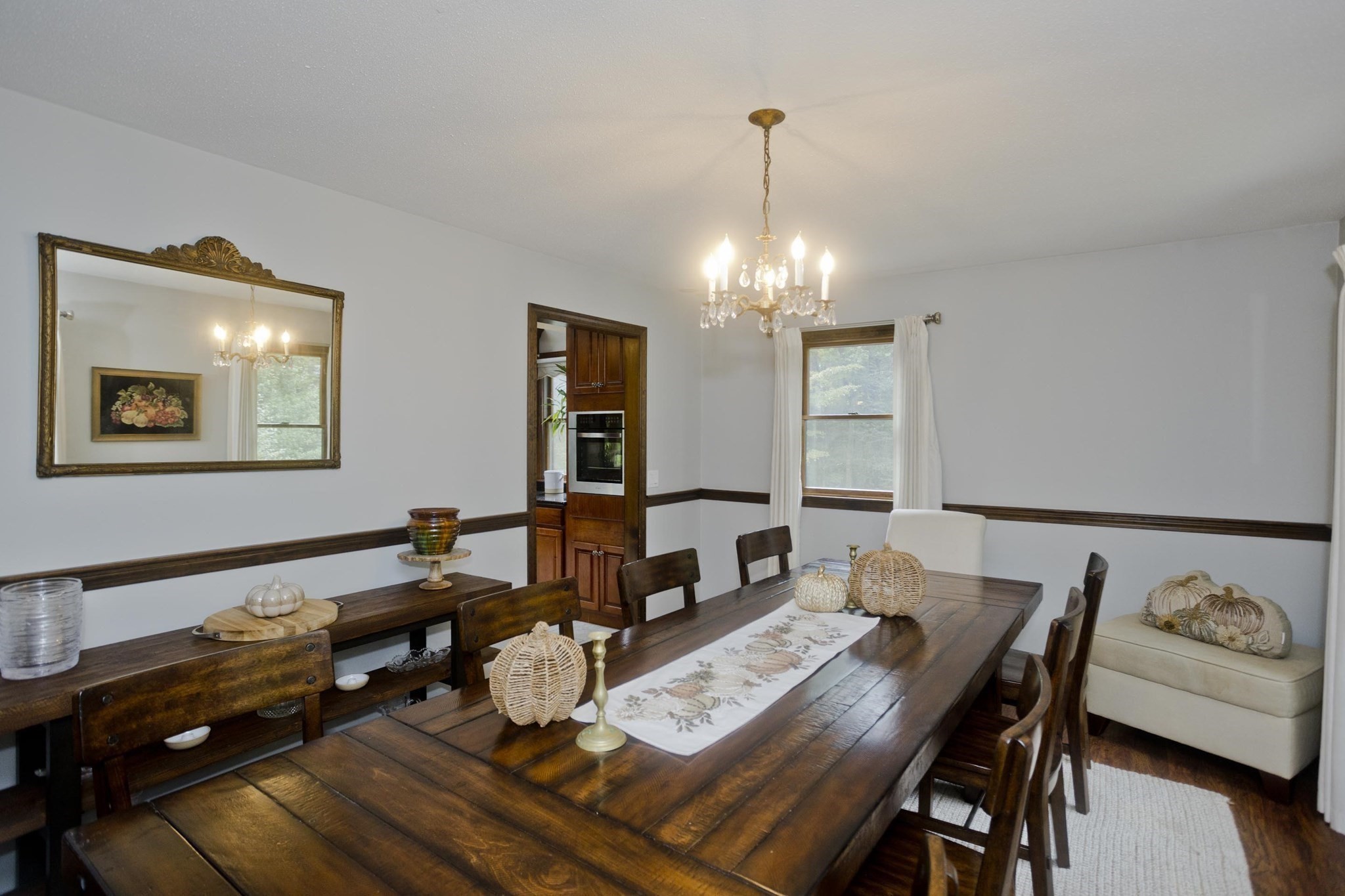 Dining room with a dark wood table, crystal chandelier, built-in oven cabinet, and curtained window.