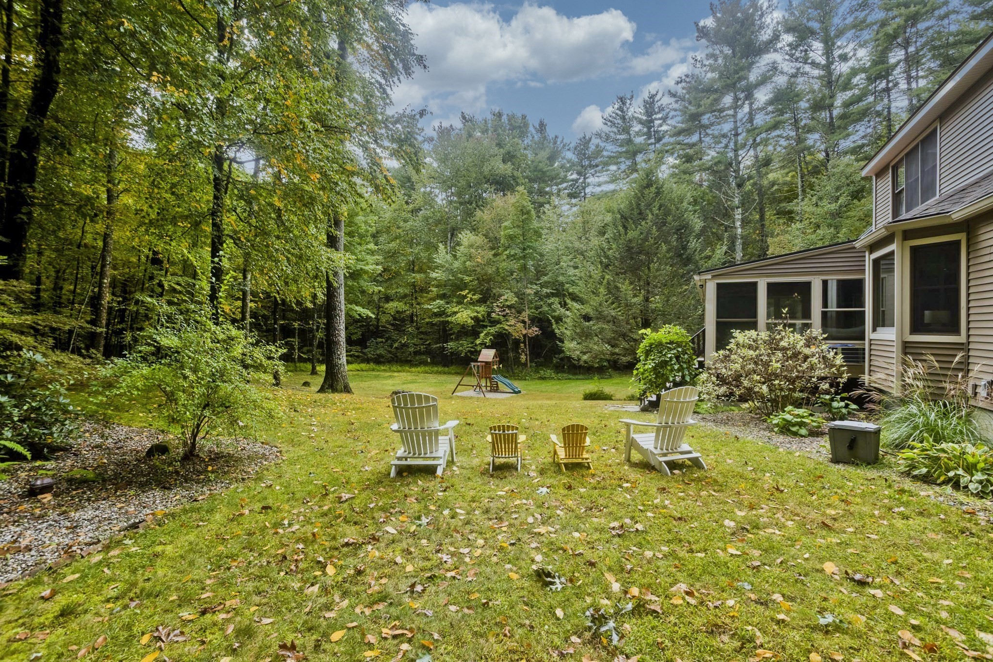 Wooded backyard with lawn chairs and a playset beside the home's screened porch.