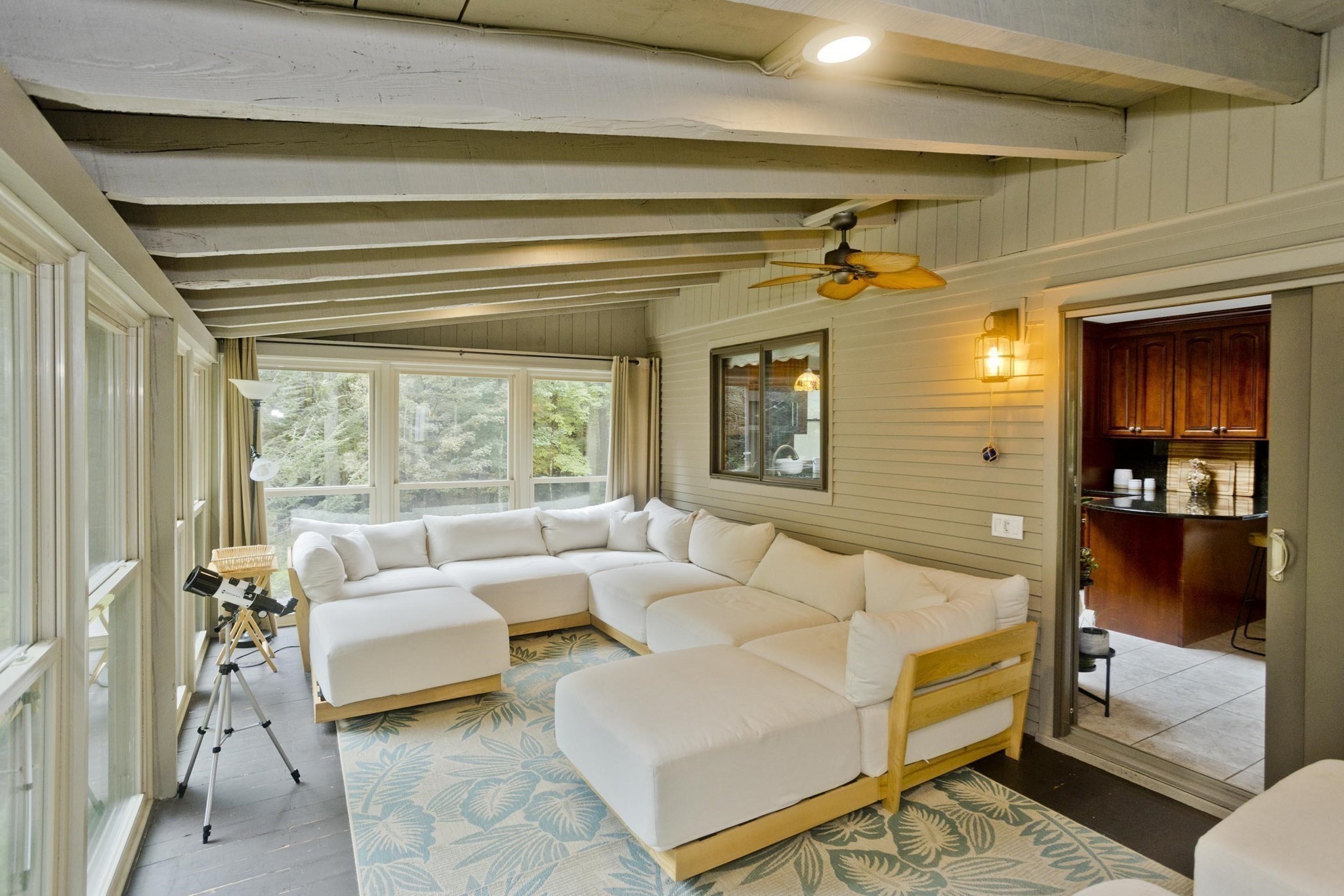 Sunroom with a white sectional, blue leaf-patterned rug, and wide windows overlooking trees.