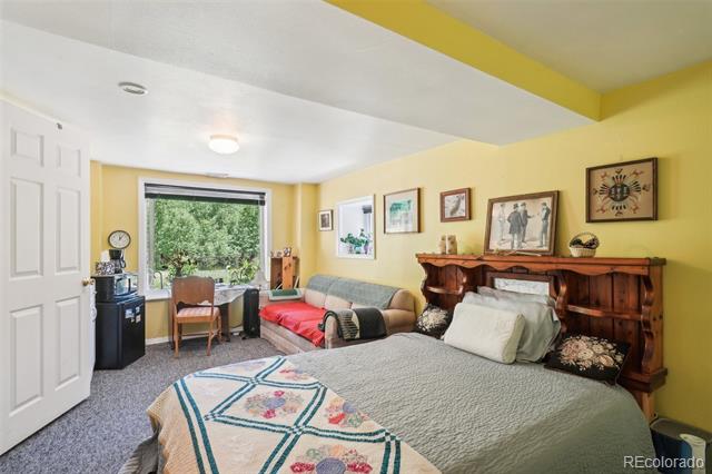 Bedroom with a carved wooden headboard, yellow walls, and a window overlooking greenery.
