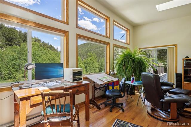 Home office with tall wood-trimmed windows overlooking trees and two workspaces.