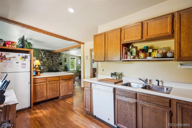 Kitchen with wood cabinetry, a double-basin sink, and hardwood floors opening to a living area with a stone fireplace.