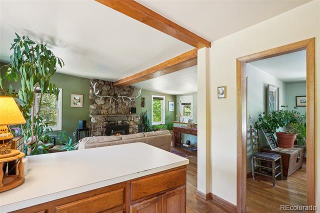 Open kitchen and living room with a stone fireplace, exposed beams, and a white peninsula.