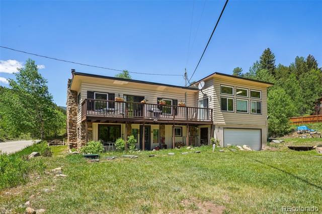 Rear of a two-story home with a long balcony, stone chimney, and attached garage.