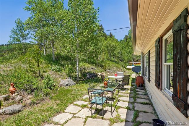 Stone patio beside a log-sided home, with outdoor dining furniture and a wooded hillside.