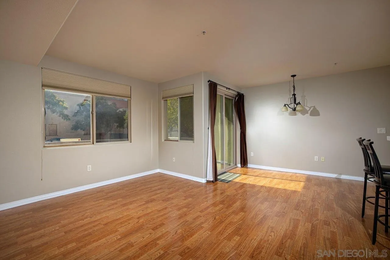 Open living and dining area with wood flooring, multiple windows, and a curtained sliding glass door.