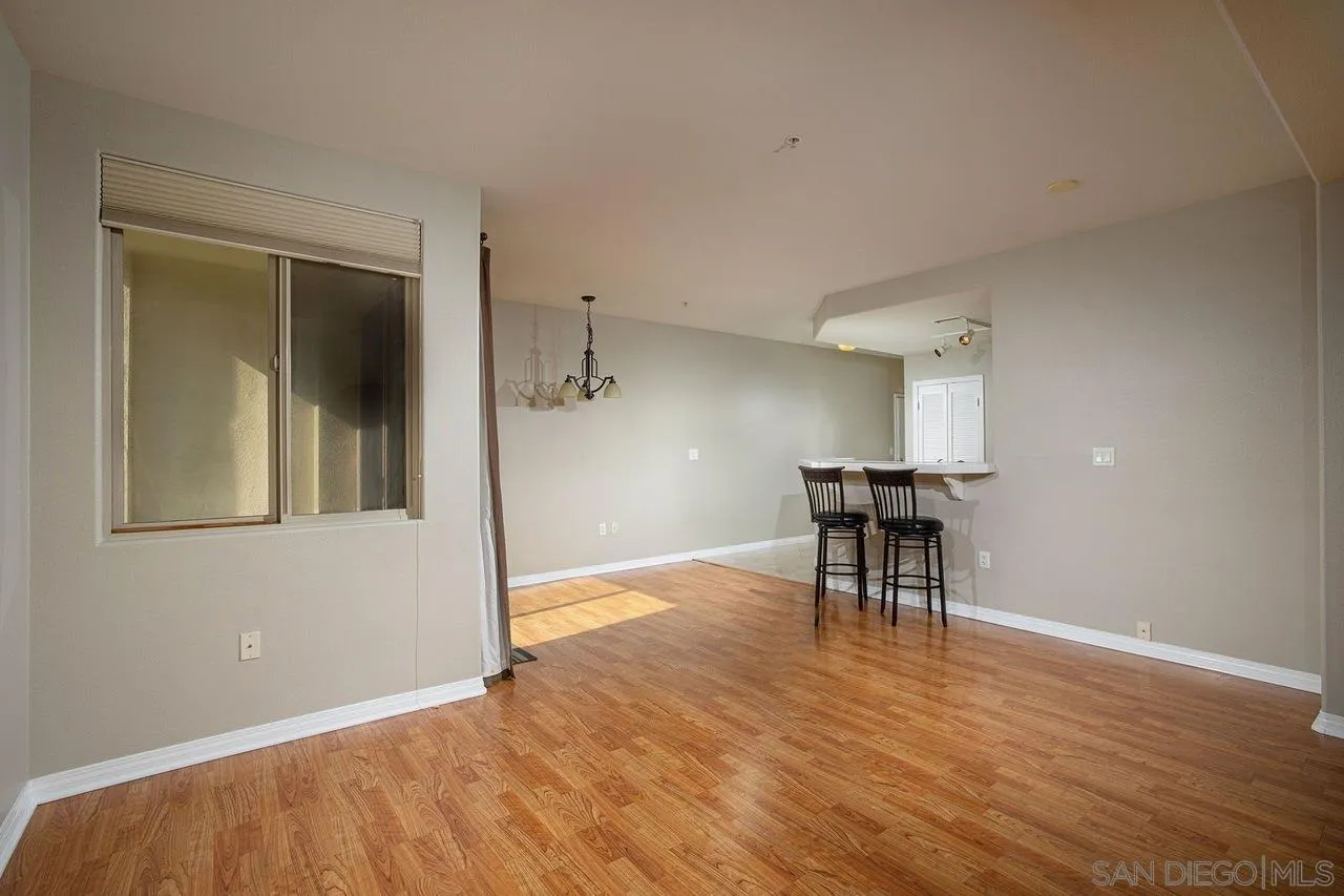 Open living and dining area with wood flooring, a window, and a breakfast bar with two stools.