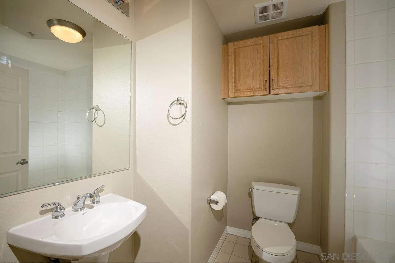Bathroom with a white sink, large mirror, toilet, and overhead wooden cabinets.