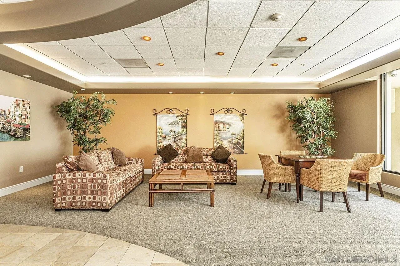 Furnished condo lounge with patterned sofas, a coffee table, and a wicker dining set.
