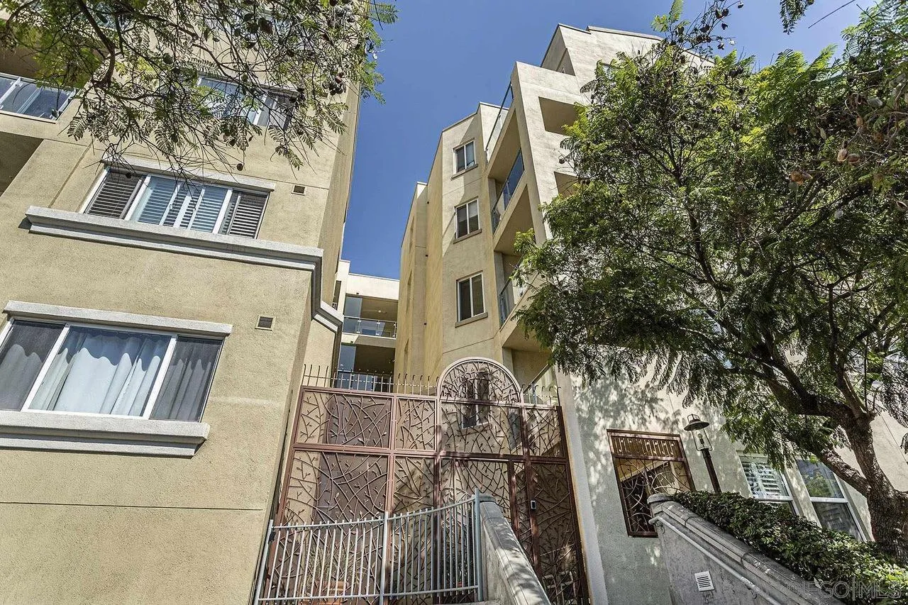 Condominium exterior with an ornate gated entrance, balconies, and leafy trees.