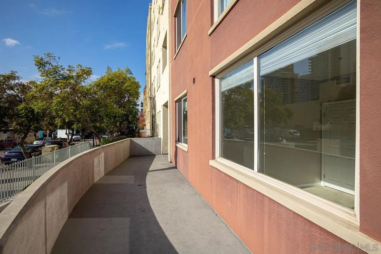Condo patio beside a salmon-colored exterior wall with broad windows and a low curved wall.