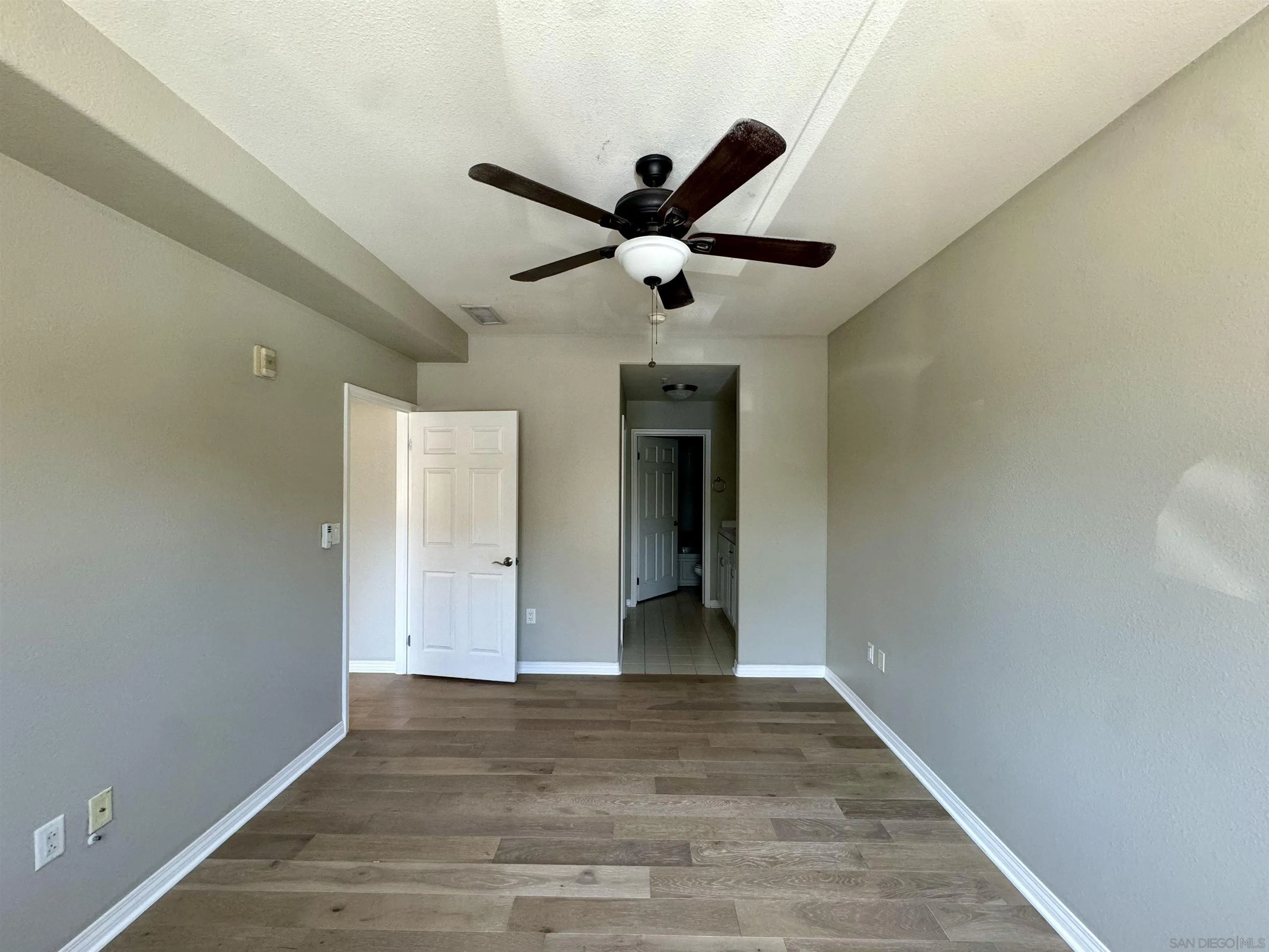 Vacant room with wood-look flooring, gray walls, and a dark ceiling fan with light.