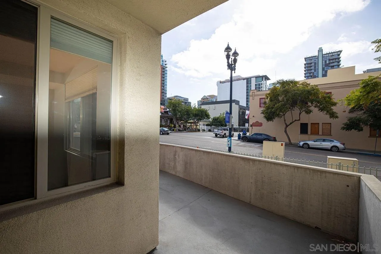 Concrete balcony overlooking a downtown street with parked cars, trees, and mid-rise buildings.