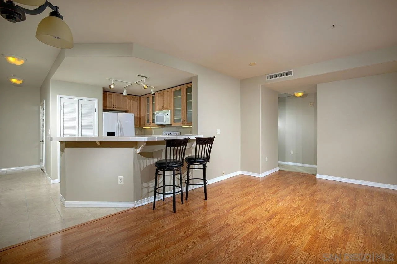 Open kitchen and living area with wood floors, a breakfast bar, and two black stools.