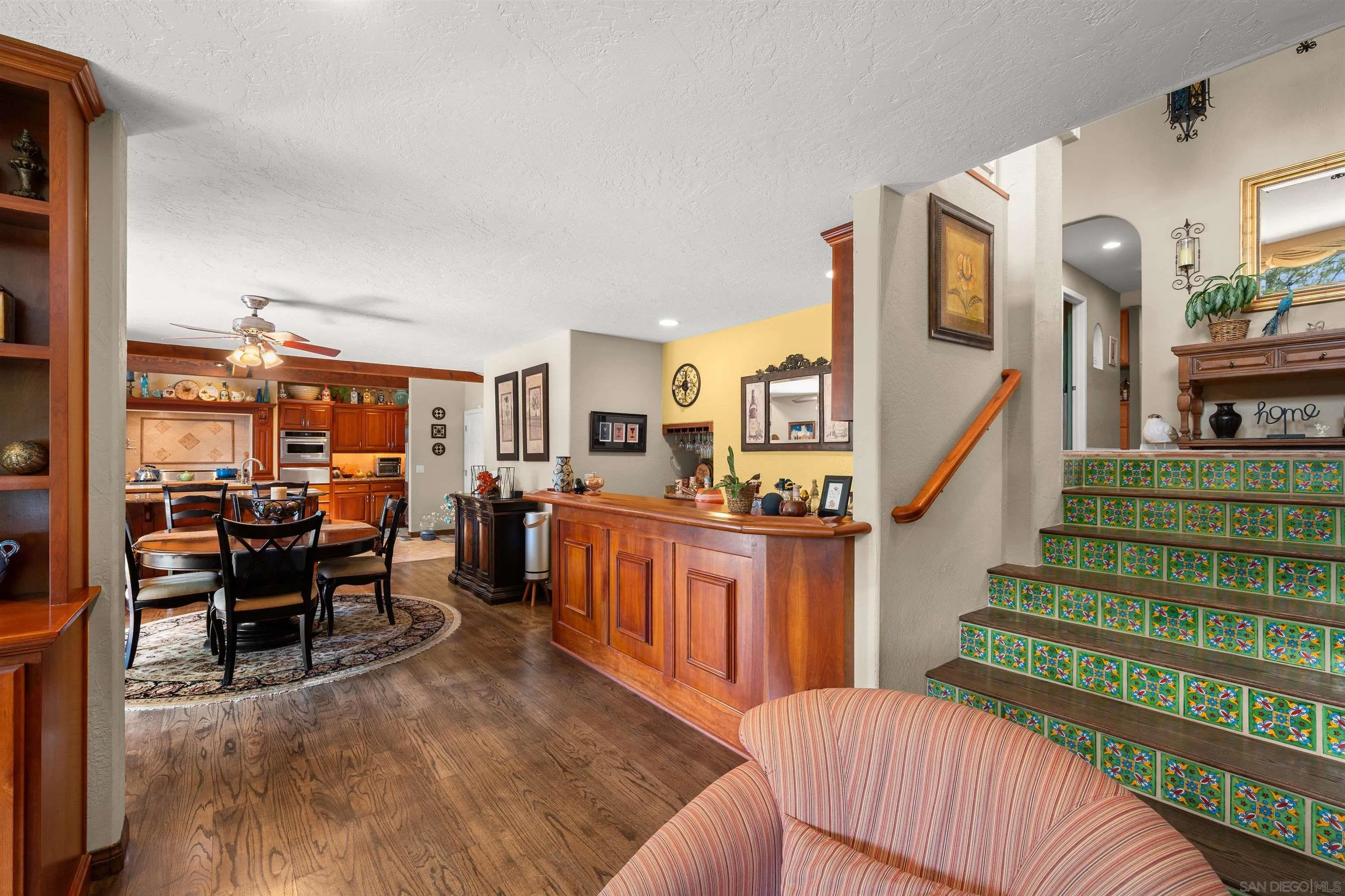 Dining area and kitchen with wood cabinetry beside a staircase with colorful tile risers.