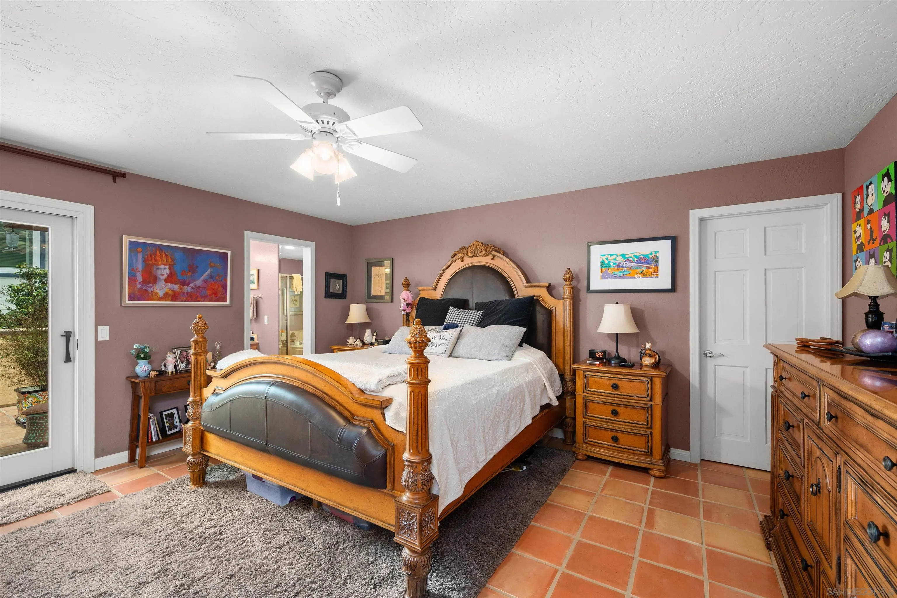 Bedroom with an ornate carved wooden bed, mauve walls, and terracotta tile floor.